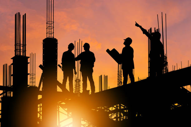 Silhouette of Engineer and worker on building site, construction site at sunset in evening time.